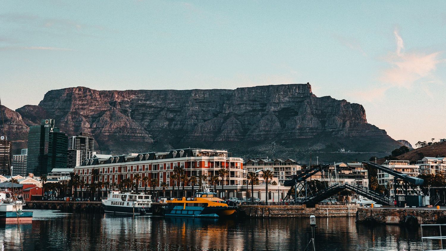 Panoramic view of Cape Town's Table Mountain and waterfront with boats in harbor at sunset.