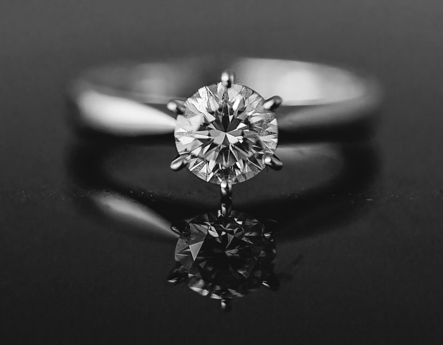 A brilliant solitaire diamond engagement ring with six prongs reflects elegantly on a mirrored surface.