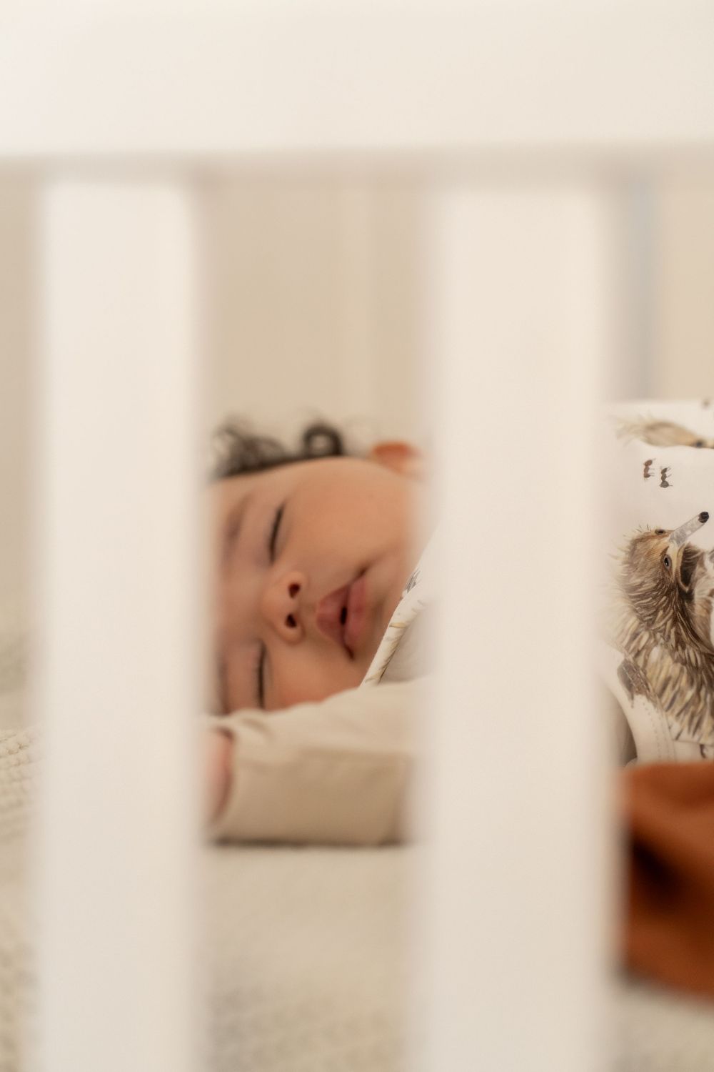 A peaceful sleeping moment captured through white crib bars in soft natural lighting.