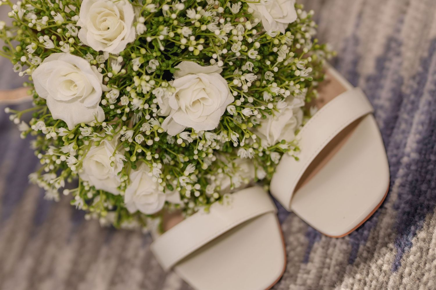 White roses and baby's breath bouquet arranged next to cream-colored bridal shoes.