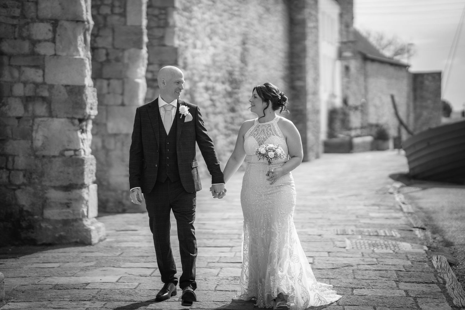 Wedding couple walking hand in hand along rustic stone pathway in black and white.