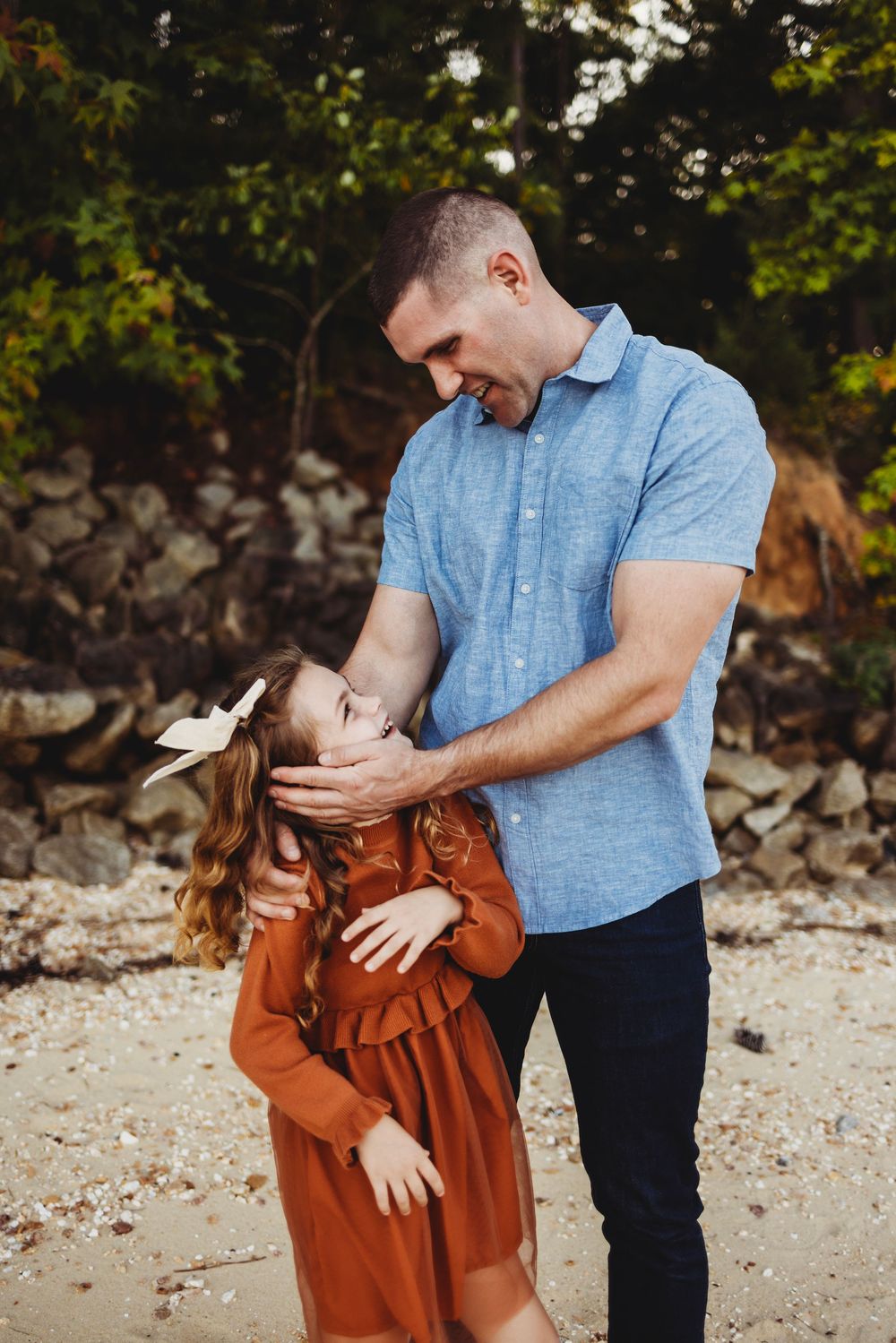A tender moment shared between an adult and child in a blue shirt and rust-colored dress outdoors by stone wall.