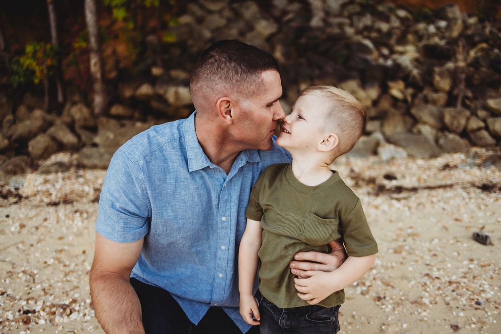 A tender moment between adult and child in denim shirt and olive green t-shirt sitting outdoors against a rocky backdrop.