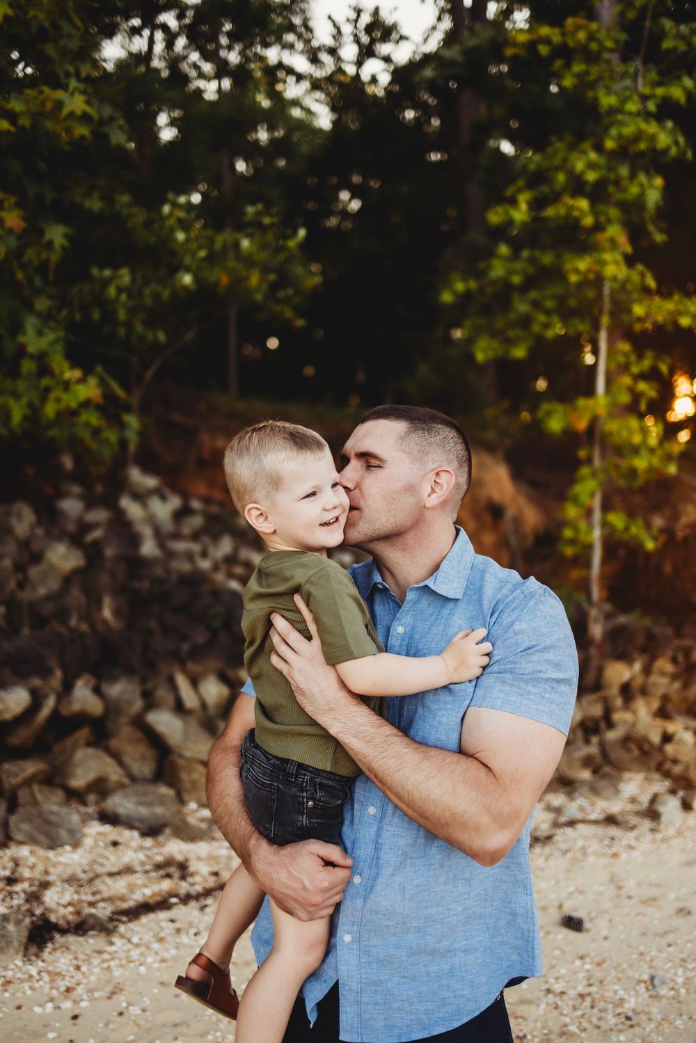 A tender moment captured between parent and child on a rocky beach with trees in the background.