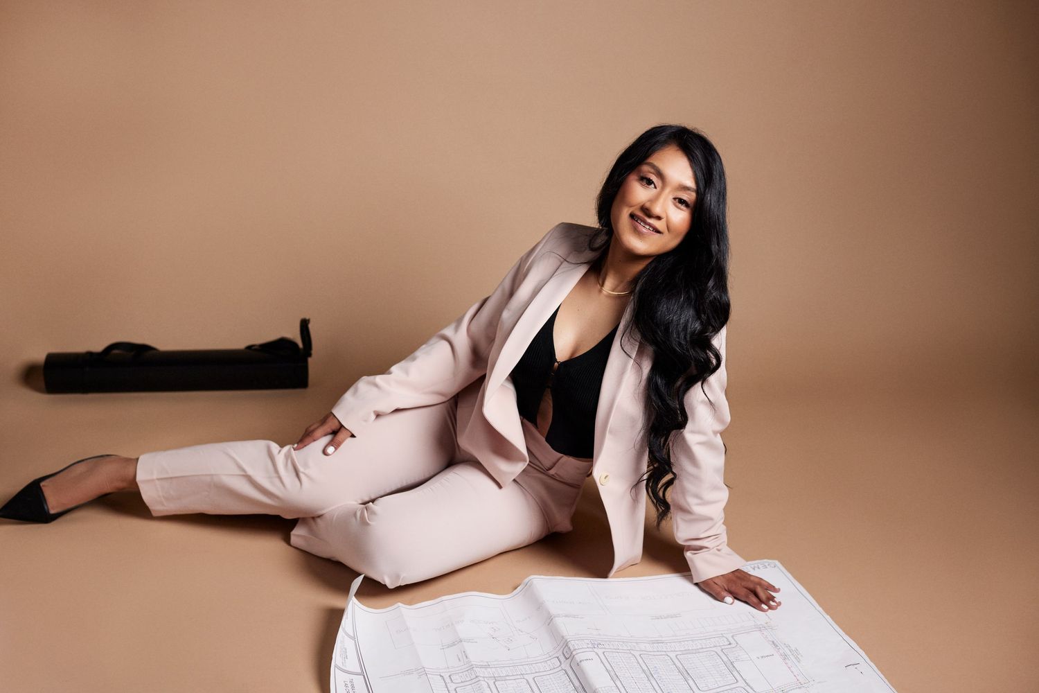 Woman in pink outfit poses with architectural plans in studio setting.