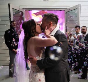 Newlyweds share their first kiss surrounded by floating bubbles and purple lighting at their reception.