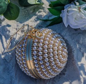Pearl-encrusted gold spherical wedding accessory or ornament displayed with white roses and greenery.