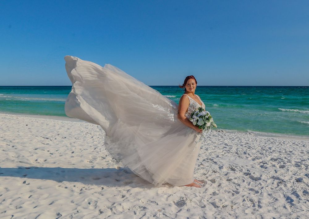 A flowing dress catches the ocean breeze on a pristine white sand beach with turquoise waters.