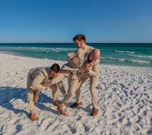 Groomsmen in light colored suits playfully posing on a pristine white sand beach.