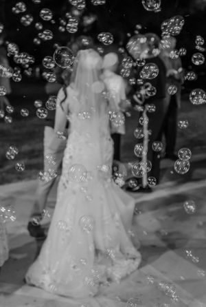 A dreamy black and white wedding photo with floating soap bubbles surrounding a bride in her elegant gown.