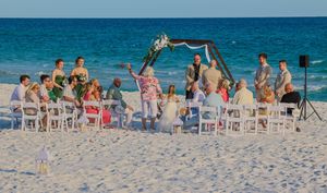 A beachside wedding ceremony setup with white chairs on sandy shores against turquoise ocean waters.