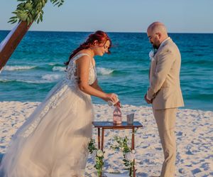 A couple performs a unity sand ceremony during their beach wedding against turquoise ocean waters.