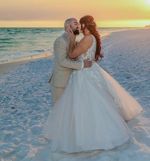 A romantic beach wedding scene with couple embracing at sunset on white sandy shore.