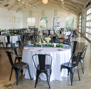 Modern wedding reception venue with white tablecloths and black metal chairs in an industrial-chic space.