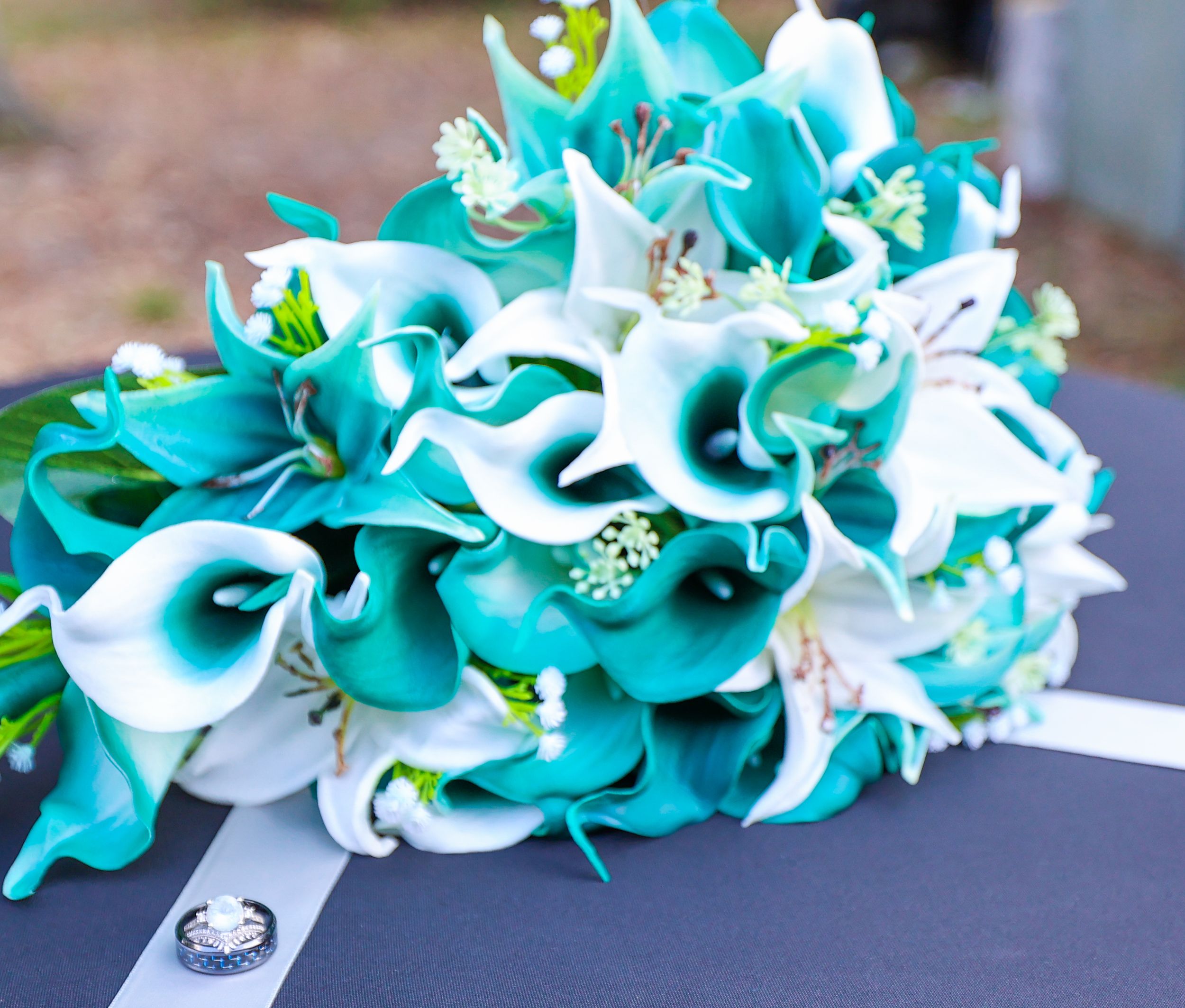 A stunning bridal bouquet featuring teal and white calla lilies with crystal accents on a dark background.
