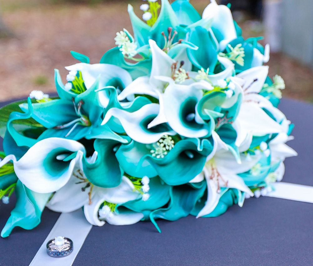 A stunning bridal bouquet featuring teal and white calla lilies with crystal accents on a dark background.