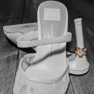 White bridal sandals and wedding ring displayed on dark wooden surface in monochrome style.