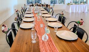 Long wooden dining table set with white plates and black chairs, decorated with a coral table runner.