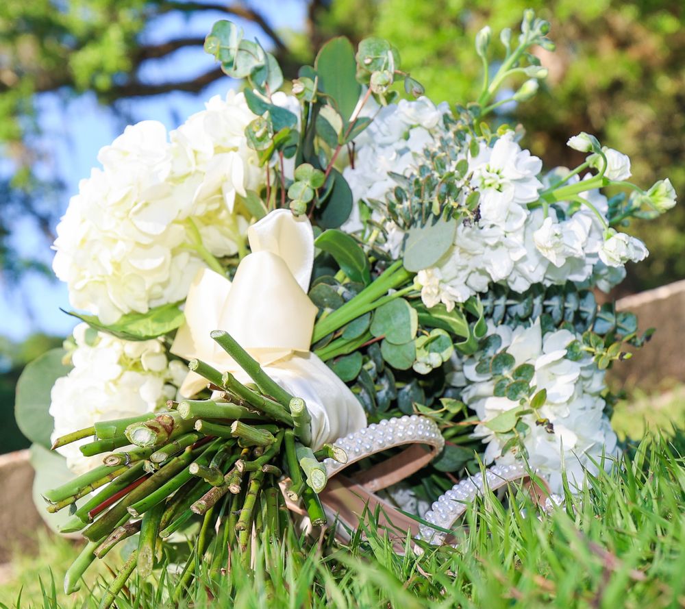 Elegant white wedding bouquet with roses, hydrangeas and greenery arranged on grass outdoors.