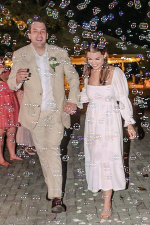 A couple in formal attire walking together amid floating bubbles at an evening celebration.