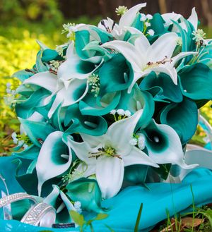 A stunning wedding bouquet featuring teal calla lilies and white lilies with delicate baby's breath accents.
