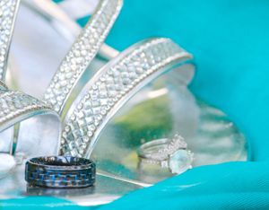Wedding rings and bridal accessories featuring crystal-encrusted shoes and jewelry on turquoise background.