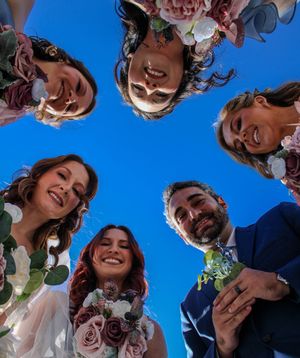 Group photo from below showing happy wedding party looking down at camera against blue sky.
