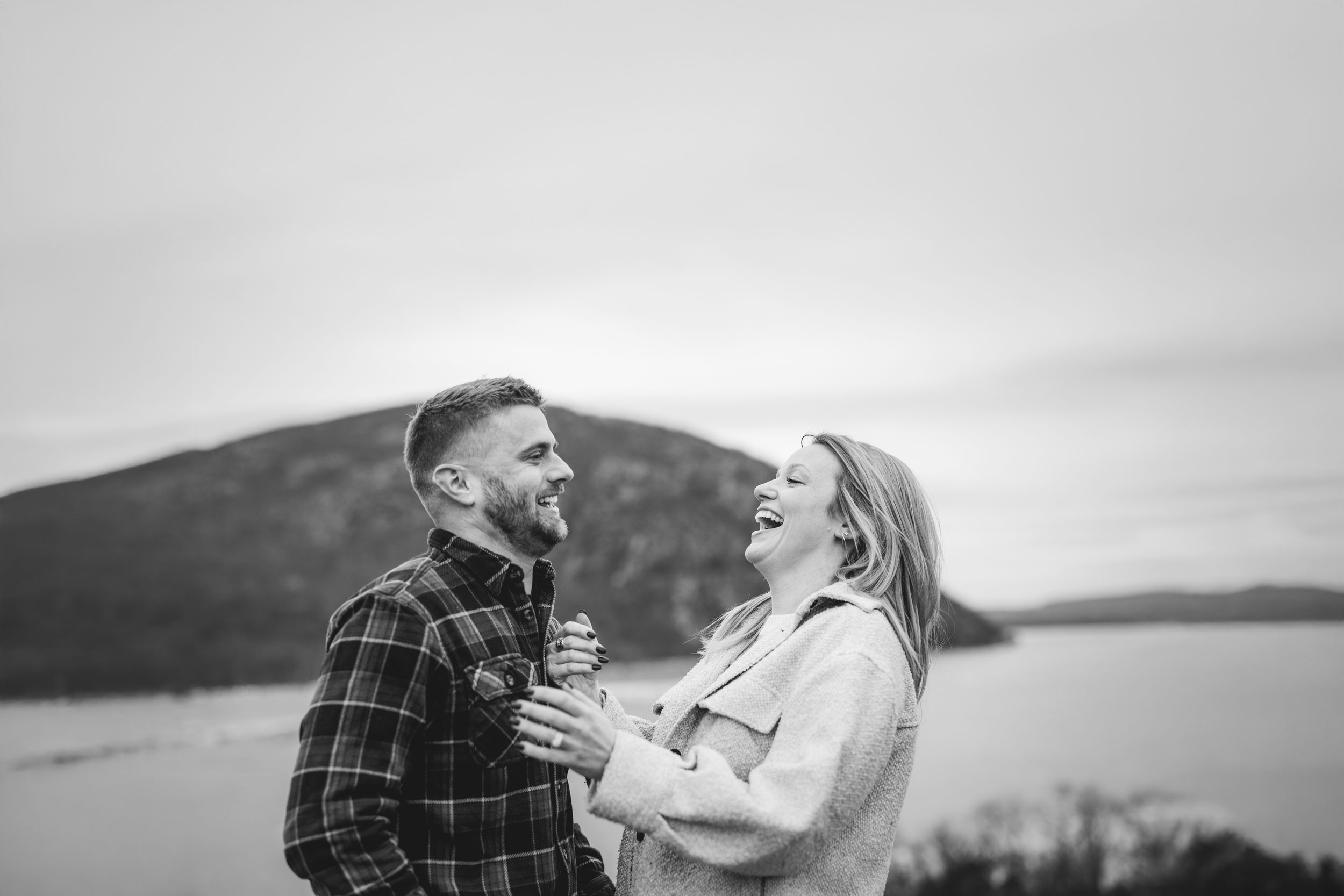 Couple embraces on a rocky beach with scenic water and mountain views in the background.