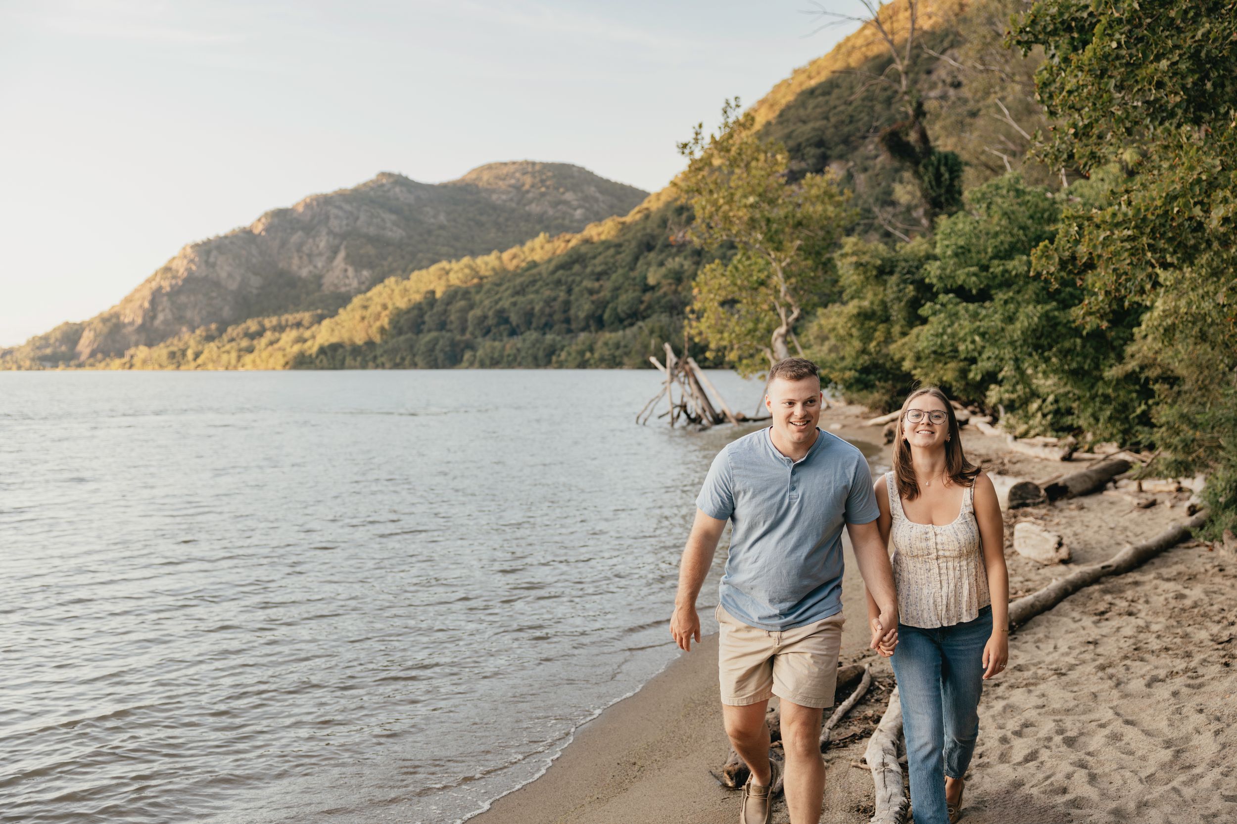 Couple walking along scenic mountain lake shoreline during golden sunset hour.