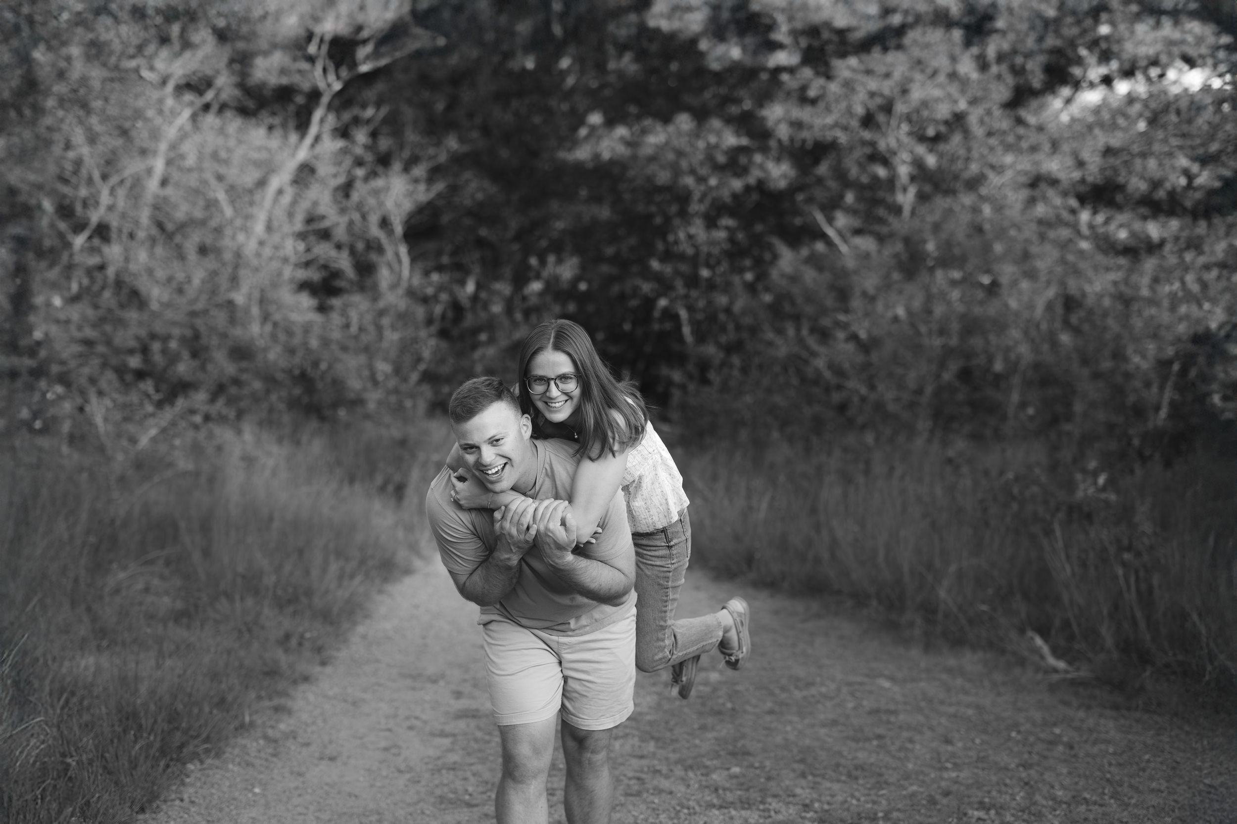 A couple walks together through a wooded path while sharing a tender romantic moment.