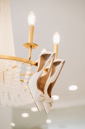 White bridal heels hanging elegantly on a gold crystal chandelier in soft lighting.