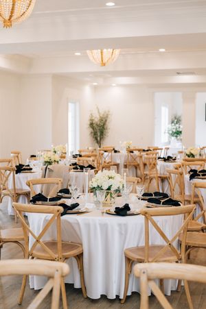 Elegant wedding reception venue with round tables set with white linens, wooden cross-back chairs and floral centerpieces.