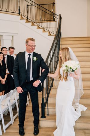 A wedding ceremony on elegant beige stone stairs with black metal railings and white folding chairs.