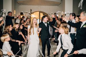 Wedding party celebrates with sparklers lining the walkway as couple exits reception through grand archway.