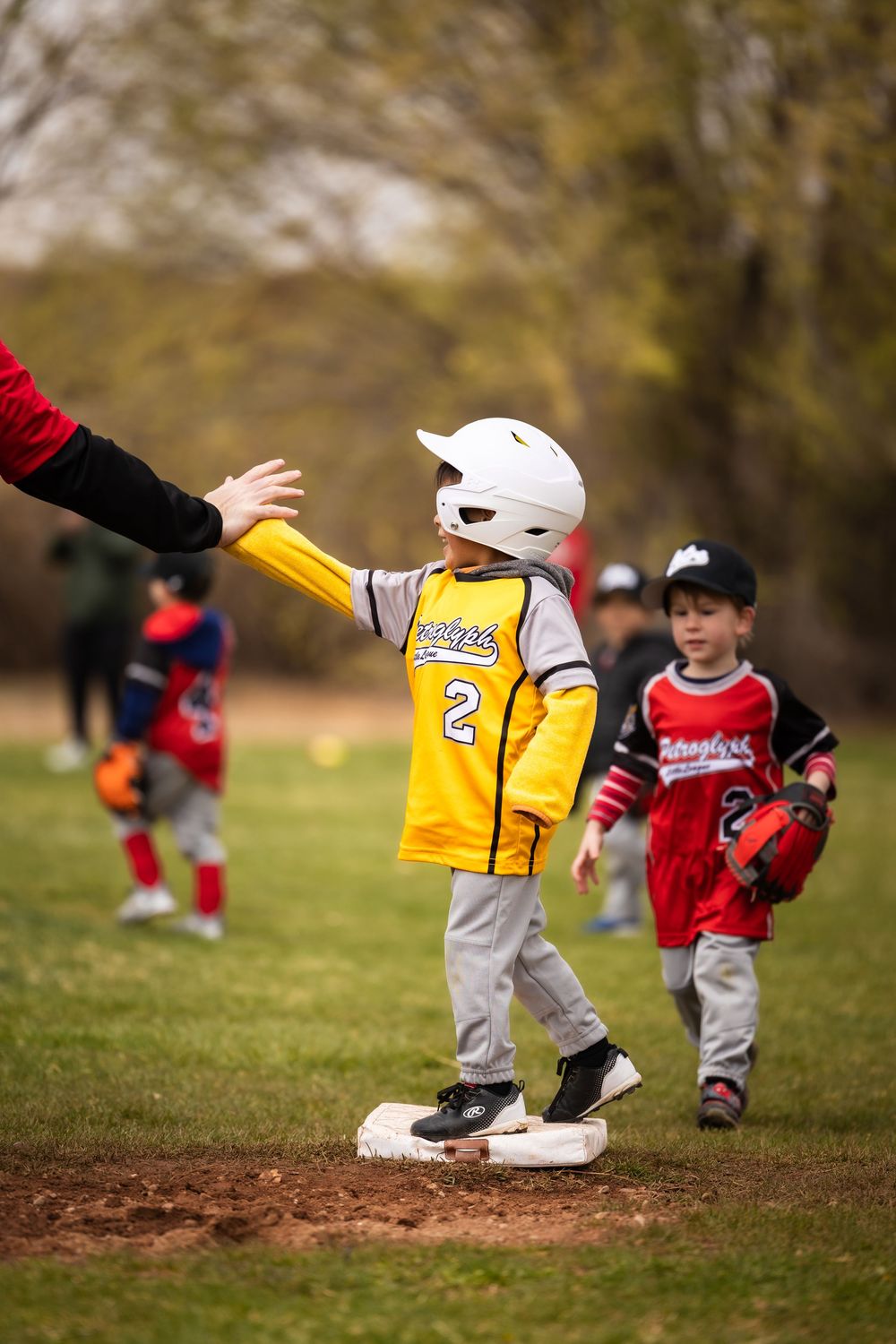 Teeball player giving high five to coach at first base. Sports photography by Memorari Portrait in Albuquerque, New Mexico