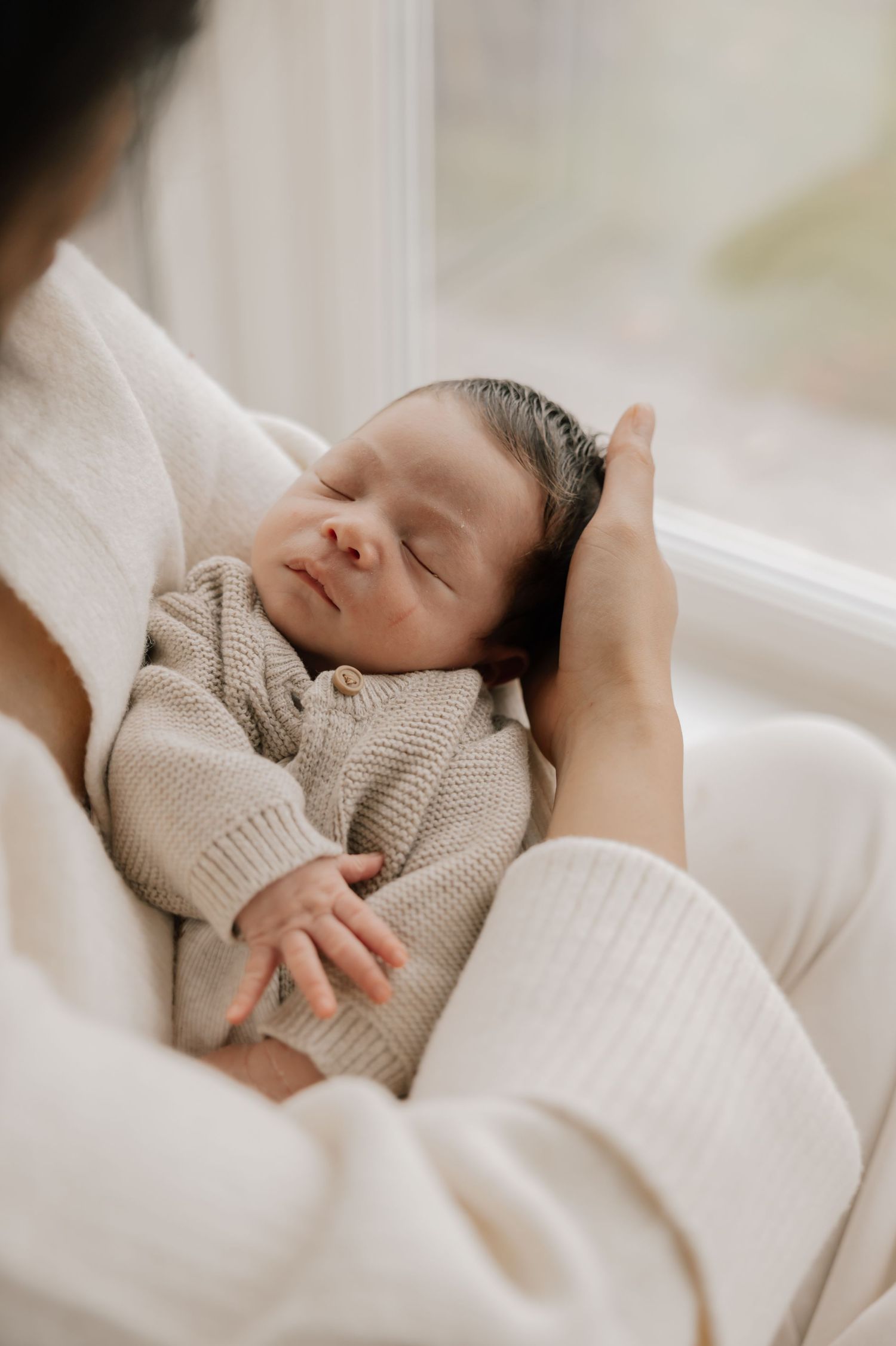 Peaceful sleeping newborn baby wearing cream-colored clothing rests on soft white bedding.