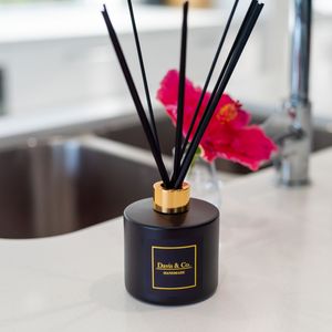 Black reed diffuser with gold accent and red flower decoration.