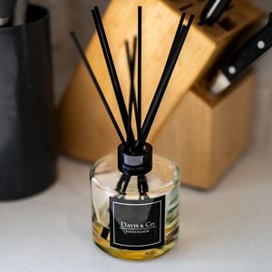 Reed diffuser bottle from Dawn & Co displaying black reeds in amber liquid against wooden background.