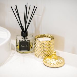 Reed diffuser and gold decorative candle holder arranged on white surface.