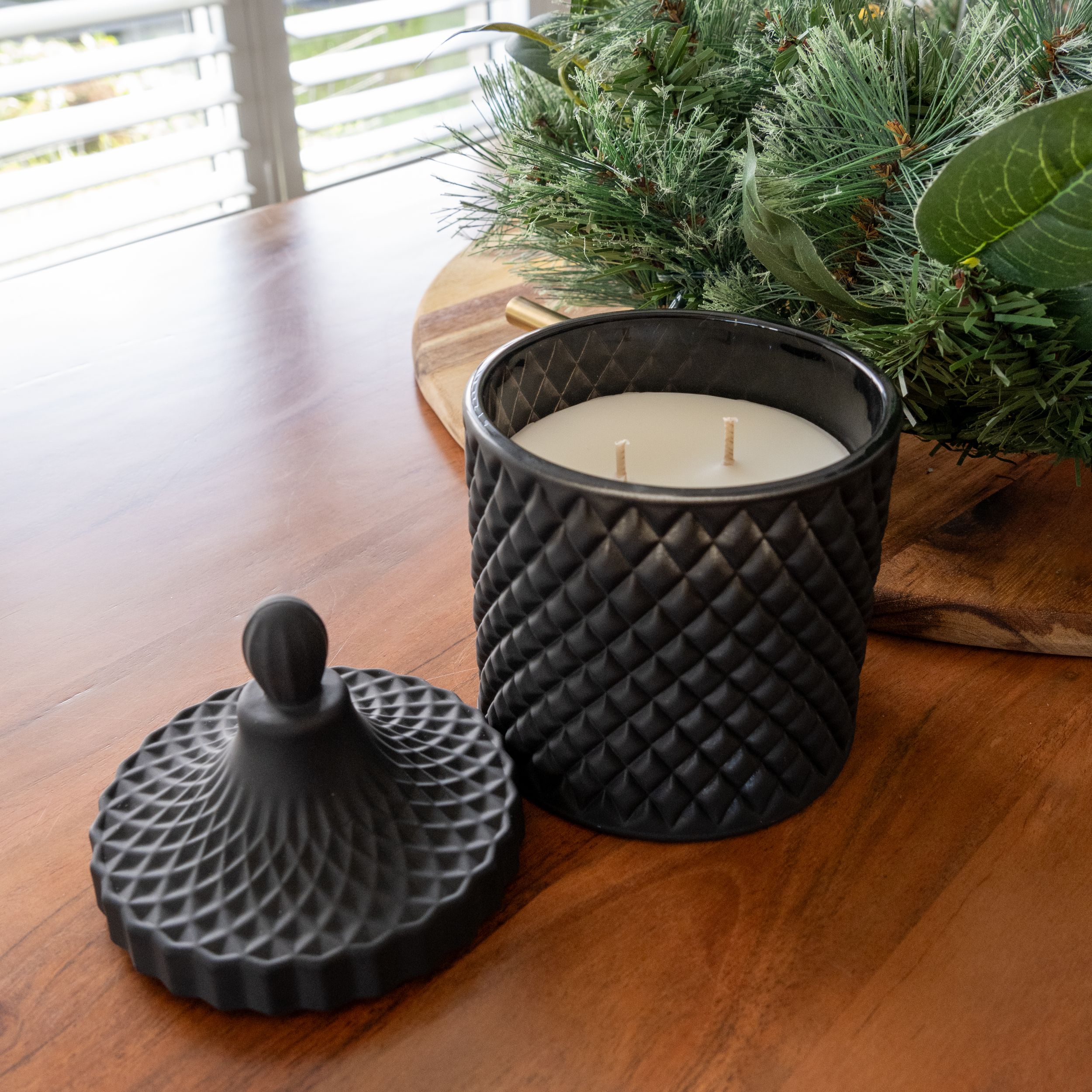 Black textured candle holder with geometric pattern lid on wooden table.