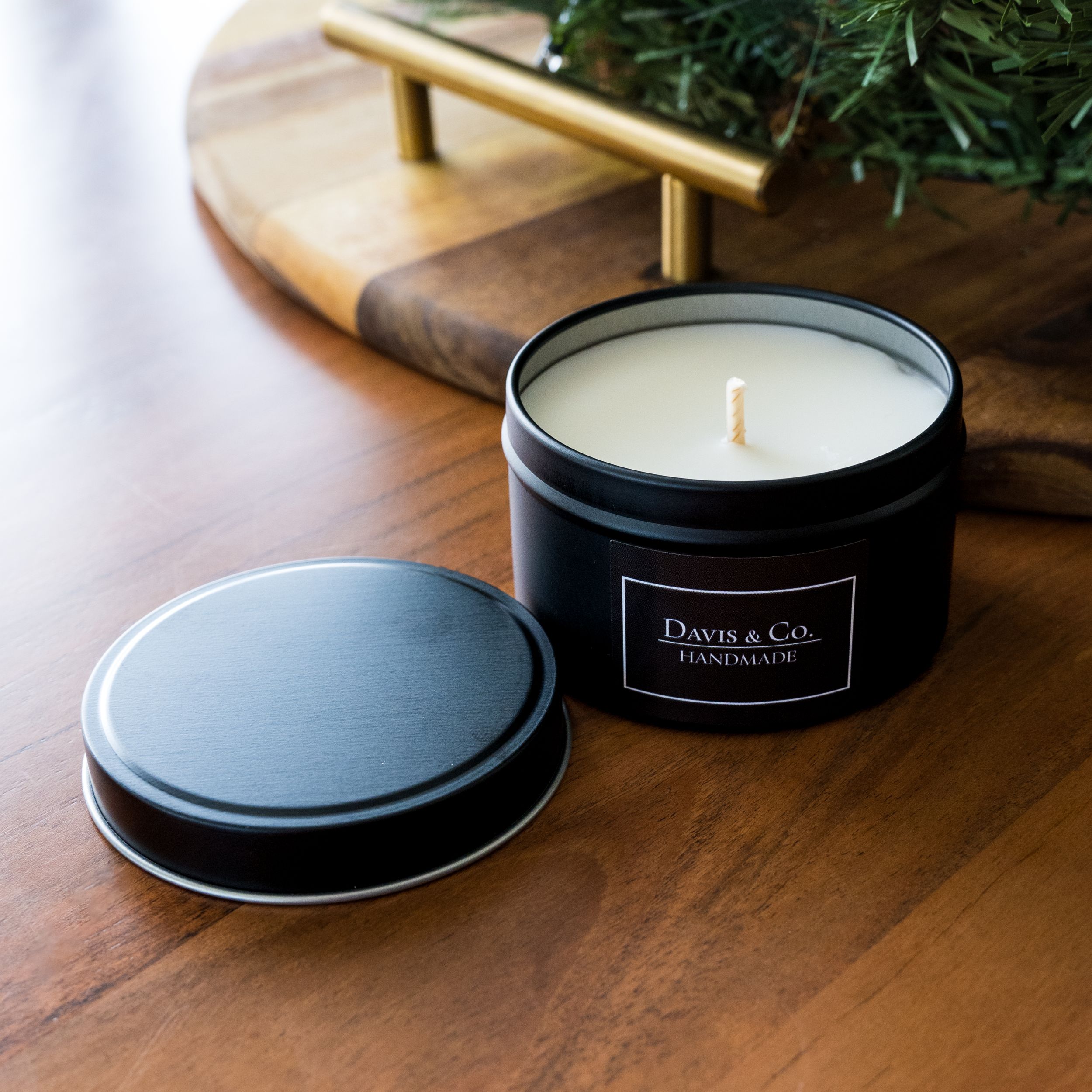 Black luxury scented candle in tin container on wooden surface.
