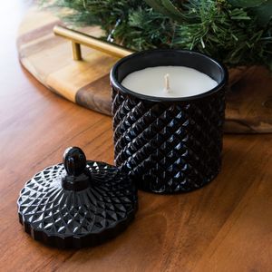 Matte black geometric patterned candle holder with matching lid on wooden surface.