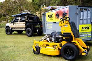 Commercial lawn maintenance truck and yellow stand-on mower parked on grass near trailer.