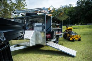 Professional landscaping equipment trailer with loading ramp and yellow mower.
