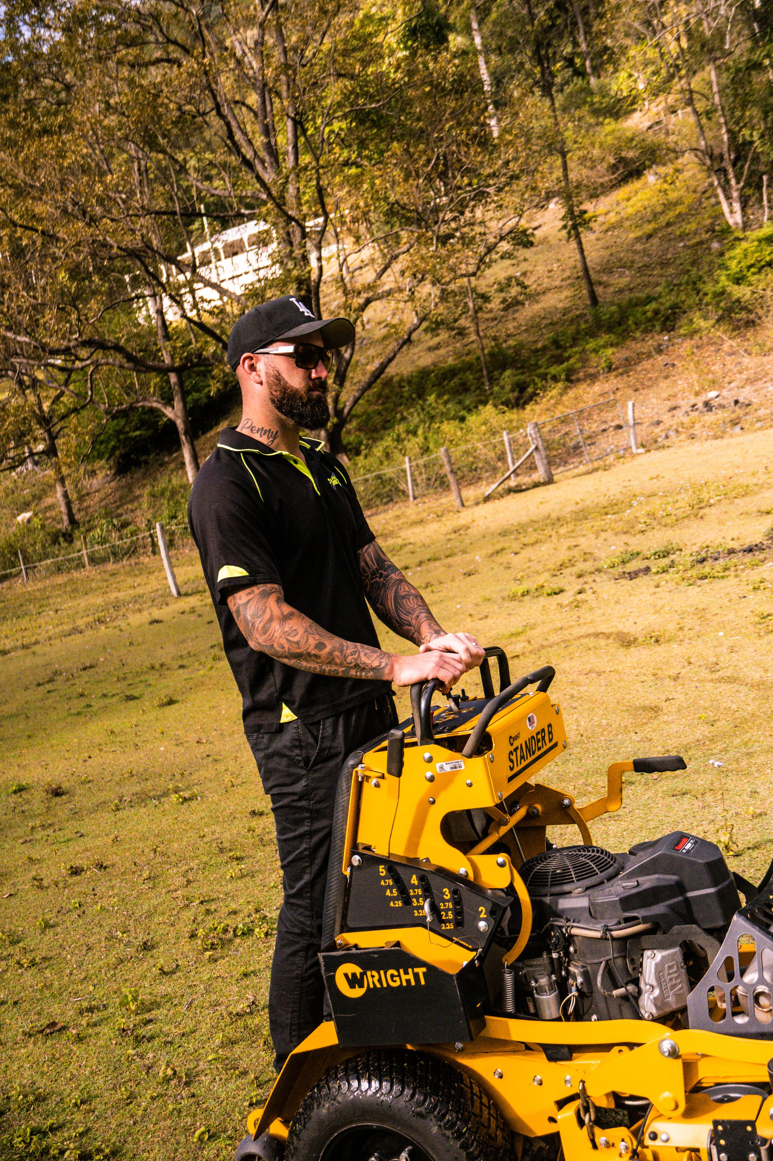 Landscaping professional with yellow stand-on mower working on hillside terrain.