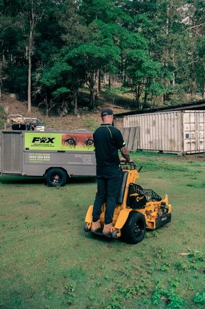 Commercial lawn maintenance worker operating yellow stand-on mower near service truck.