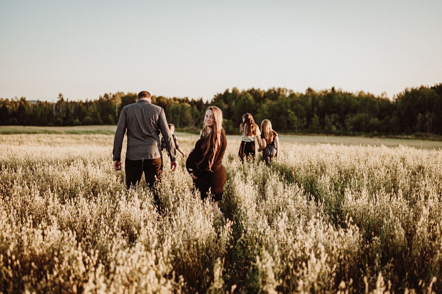 Famille marchant ensemble à travers un champ de hautes herbes baignées de soleil pendant l’heure dorée.