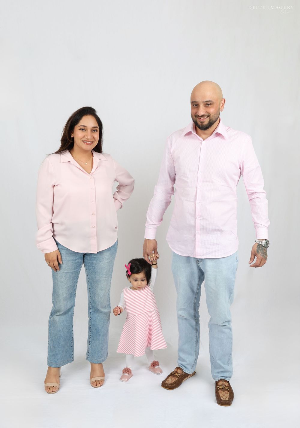 Family wearing coordinated pink and light blue outfits poses together against white background in studio setting.