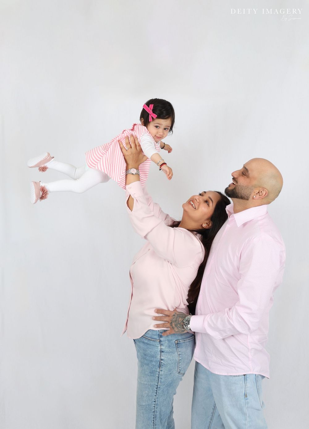 Family wearing coordinated pink and white outfits plays together against light gray studio background.