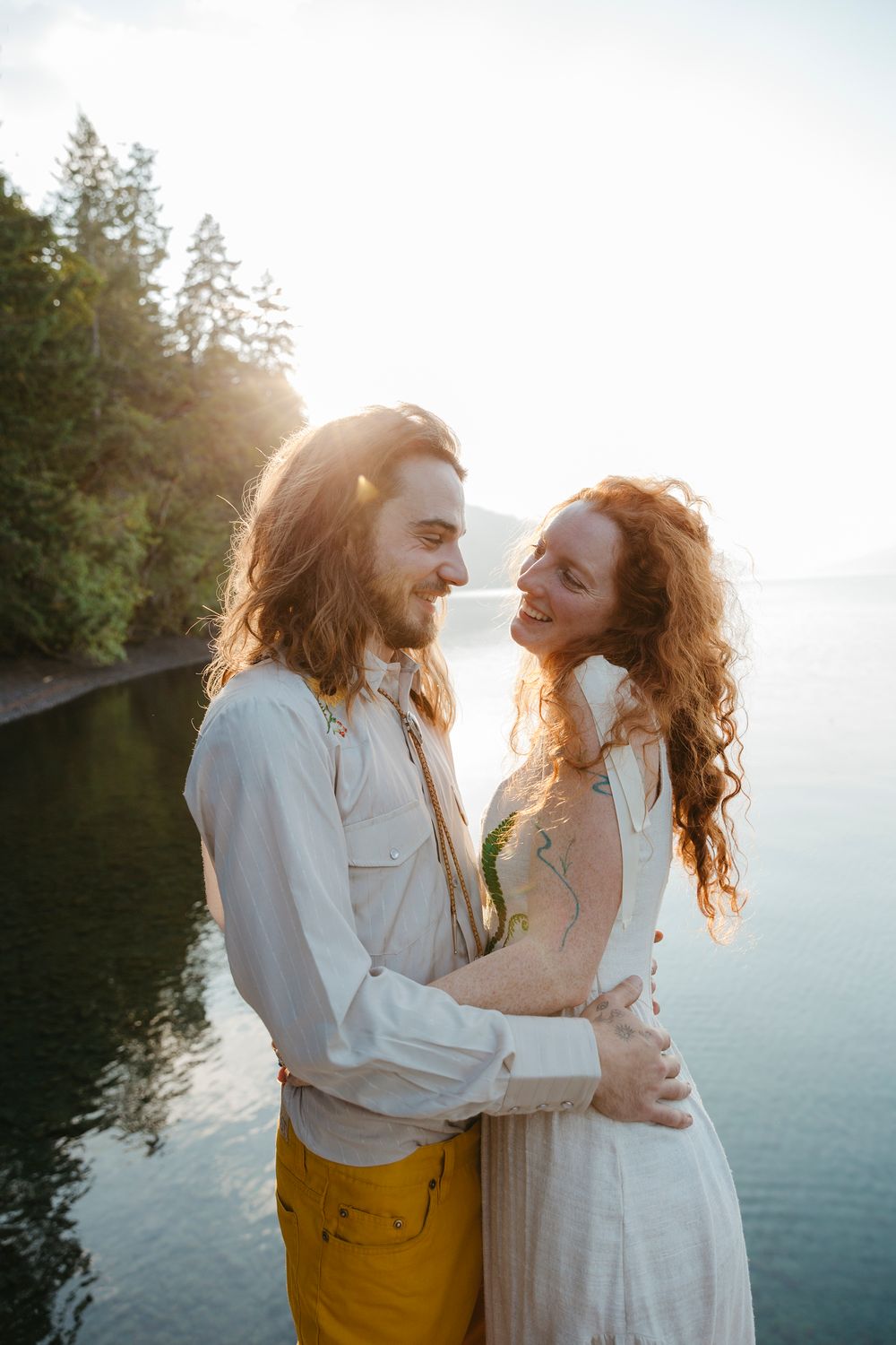 Couple in white and yellow outfits embracing by a lake during golden hour.